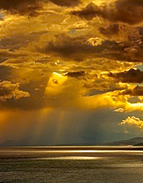 Bands of sunlight burst through clouds over the ocean